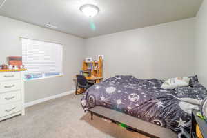 Bedroom featuring light carpet, baseboards, and a textured ceiling