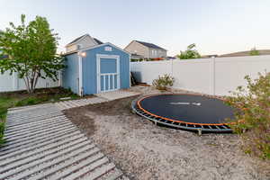 Fenced backyard with a trampoline, a storage shed, and an outdoor structure