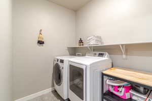 Clothes washing area with washing machine and dryer, light tile patterned floors, and baseboards