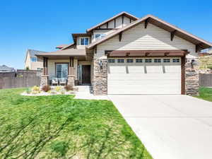 Craftsman house featuring an attached garage, stone siding, a front yard, and fence