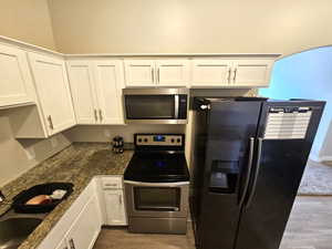 Kitchen featuring appliances with stainless steel finishes, white cabinetry, dark wood-type flooring, and dark stone counters