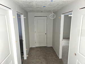 Corridor with carpet, a textured ceiling, and baseboards