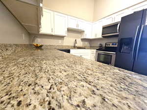 Kitchen with appliances with stainless steel finishes, white cabinetry, a sink, and light stone counters