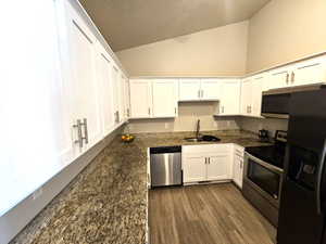 Kitchen with stainless steel appliances, a sink, white cabinets, lofted ceiling, and dark wood-type flooring