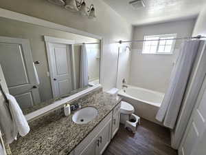 Bathroom featuring a textured ceiling, wood finished floors, shower / tub combo with curtain, toilet, and vanity