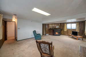 Living room featuring light carpet, a warm lit fireplace, and wood walls