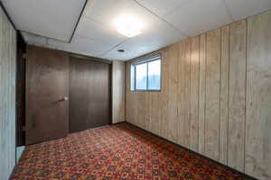 Unfurnished bedroom with wooden walls, a drop ceiling, a closet, and carpet floors