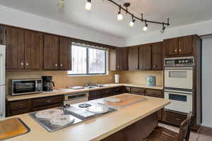 Kitchen with white appliances, a sink, dark brown cabinets, and light countertops