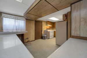 Kitchen featuring white appliances, under cabinet range hood, light flooring, wooden walls, and brown cabinetry