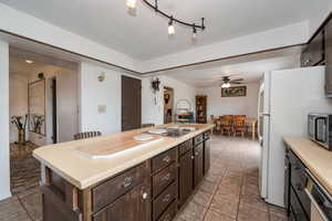Kitchen with appliances with stainless steel finishes, light countertops, ceiling fan, dark brown cabinetry, and a center island
