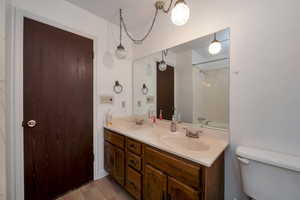 Full bath featuring toilet, double vanity, and wood finished floors