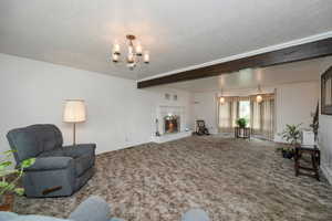 Carpeted living area with a chandelier, baseboards, a textured ceiling, and a fireplace