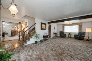 Carpeted living room with a chandelier, stairs, and baseboards