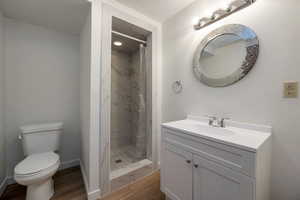 Full bath with wood finished floors, toilet, a stall shower, vanity, and baseboards