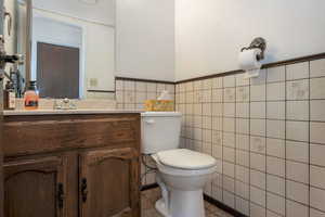 Half bath with toilet, tile walls, vanity, and a wainscoted wall