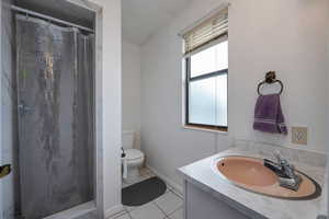 Bathroom featuring toilet, tile patterned floors, vanity, curtained shower, and baseboards