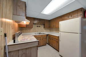Kitchen featuring freestanding refrigerator, electric range oven, light countertops, under cabinet range hood, and wooden walls