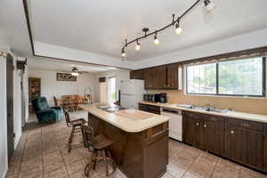 Kitchen featuring white appliances, a kitchen bar, a sink, dark brown cabinetry, and light countertops