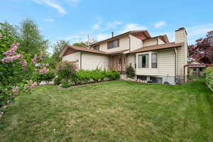 Rear view of property featuring a chimney, a yard, a garage, and roof with shingles