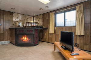 Carpeted living area with wooden walls and a warm lit fireplace