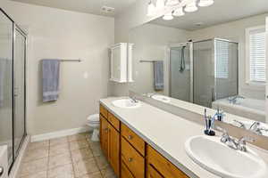 Full bathroom with a shower, tub, tile flooring, baseboards, toilet, and double vanity