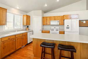 Kitchen featuring white appliances, a sink, light countertops, light wood-type flooring, and lofted ceiling
