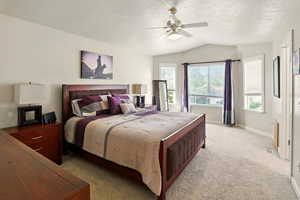 Primary bedroom with lofted ceiling, light carpet, baseboards, ceiling fan, walk-in closet, and a textured ceiling