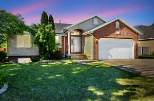 View of front of house featuring an attached garage, driveway, a front yard, and brick siding