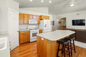 Kitchen featuring white appliances, lofted ceiling, light wood-style flooring, light countertops, and a ceiling fan