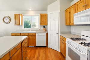 Kitchen featuring white appliances, a sink, light wood-style flooring, light countertops, and brown cabinets