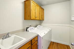 Clothes washing area with cabinet space, independent washer and dryer, a wainscoted wall, and light wood finished floors