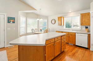 Kitchen featuring dishwasher, a sink, light wood finished floors, light countertops, and lofted ceiling