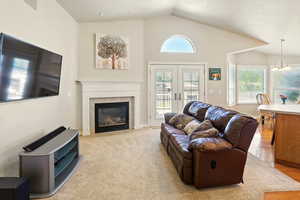 Great room featuring lofted ceiling, a tiled fireplace, a chandelier, and french doors
