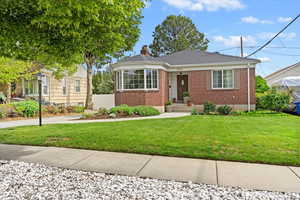 Bungalow-style home featuring brick siding, a chimney, and a front lawn