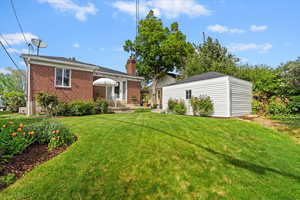 Back of the property featuring a detached garage, back yard, red brick, and a chimney, mature yard and trees.