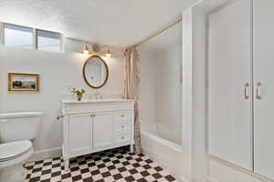 Bathroom featuring tile patterned floors, toilet, vanity, quartz counter, baseboards, and a textured ceiling with tile shower walls