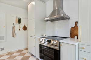 Kitchen with stainless hood, stainless steel electric range, light floors, decorative tile backsplash, and built in fridge, quartz counters