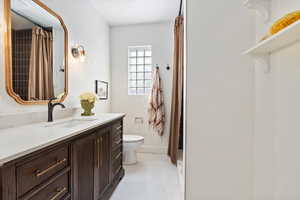 Full bathroom featuring toilet, vanity, and a tile shower with shower curtain, quartz countertop