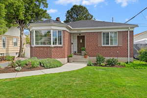 View of front facade featuring red brick siding, a front yard, a chimney, and roof with shingles