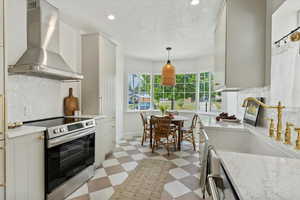 Kitchen featuring stainless steel electric range oven, light floors, stainless wall hood, a farm sink, and quartz counters, tile floors, brass faucet and knobs