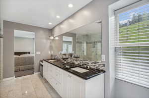 Ensuite bathroom with marble look tile flooring, a shower stall, double vanity, recessed lighting, and baseboards