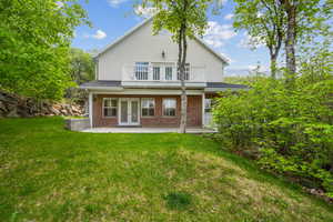 Rear view of house featuring french doors, a balcony, a patio, a yard, and brick siding