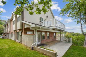 Rear view of house featuring a balcony, brick siding, stucco siding, a yard, and central AC unit