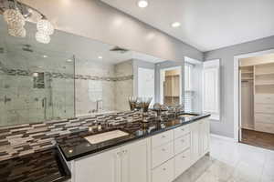 Full bath with a stall shower, baseboards, a spacious closet, double vanity, and recessed lighting