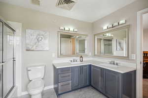 Full bath featuring marble look tiles, an enclosed shower, double vanity, toilet, and baseboards