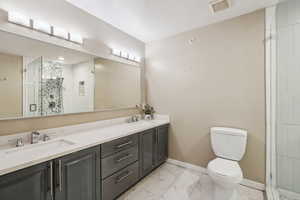 Bathroom with marble look tiles, toilet, a shower stall, baseboards, and double vanity