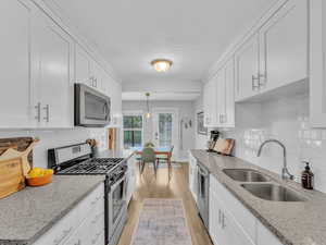 Kitchen featuring stainless steel appliances, a sink, light wood-style floors, white cabinets, and backsplash