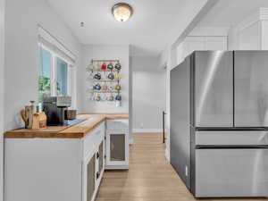 Kitchen with freestanding refrigerator, butcher block counters, light wood-style flooring, white cabinetry, and baseboards