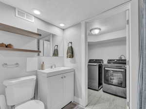 Bathroom featuring washing machine and dryer, a textured ceiling, marble finish floors, toilet, and vanity