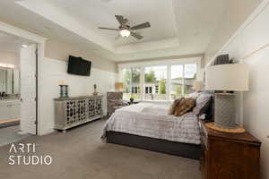 Carpeted bedroom featuring a raised ceiling, a decorative wall, connected bathroom, and a ceiling fan